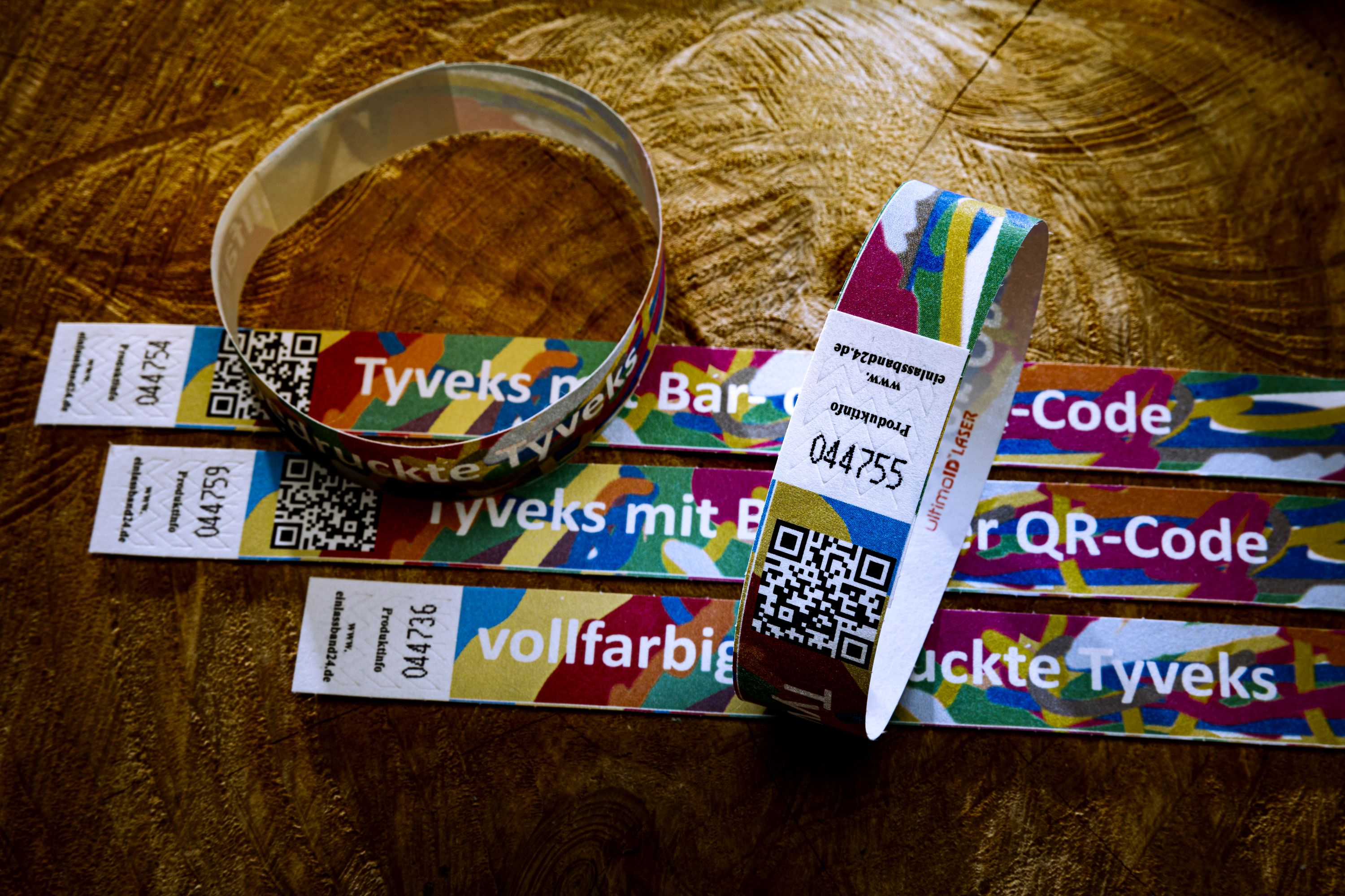 Mehrere vollfarbig bedruckte Tyvek-Armbänder mit QR-Code und Seriennummer auf Holzoberfläche