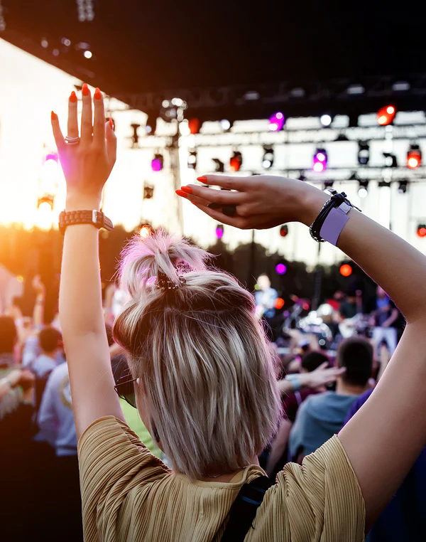 Festivalbesucherin tanzt mit erhobenen Armen vor einer Bühne im Sonnenlicht
